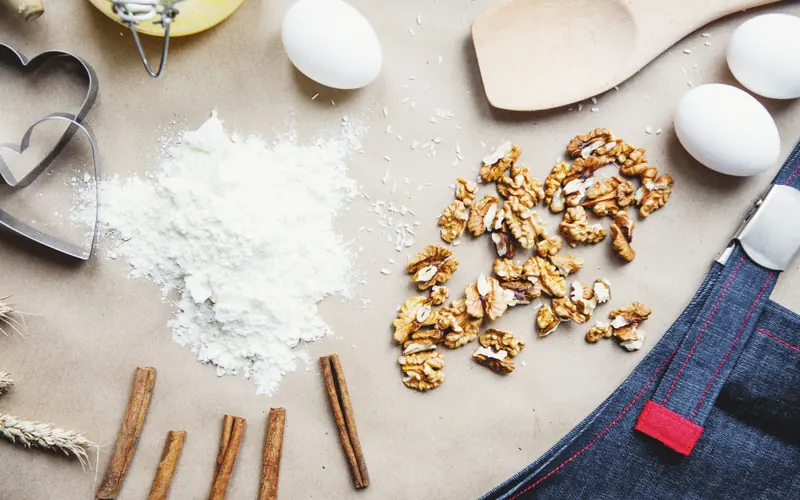 Overhead view of flour, shelled walnuts, eggs and cinnamon sticks on baking paper