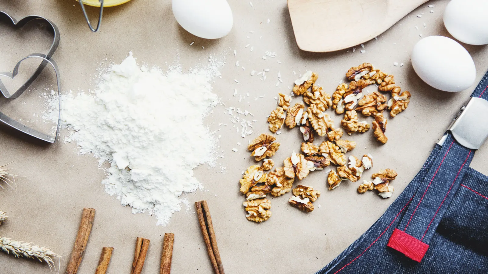 Overhead view of flour, shelled walnuts, eggs and cinnamon sticks on baking paper