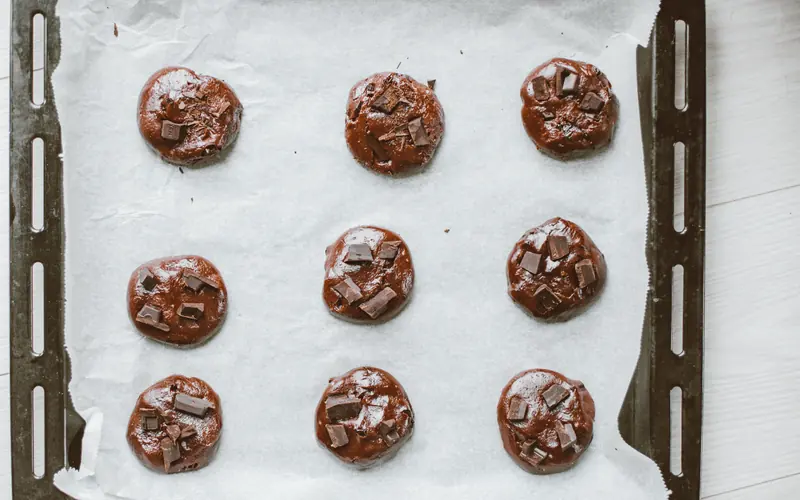 Nine evenly portioned chocolate cookie dough rounds on a parchment-lined baking sheet