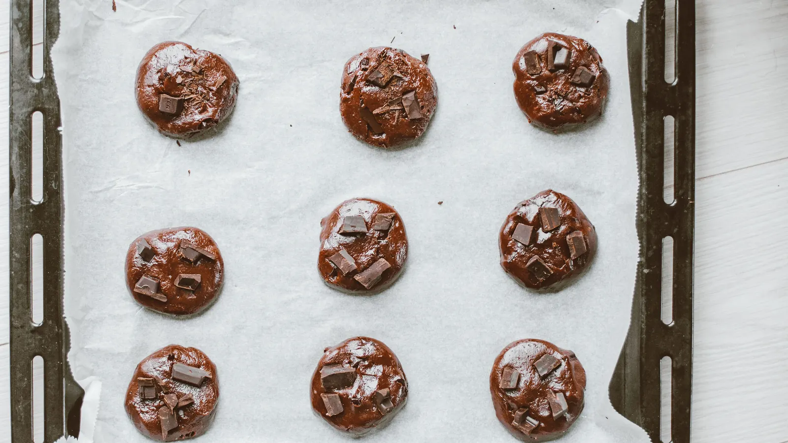 Nine evenly portioned chocolate cookie dough rounds on a parchment-lined baking sheet