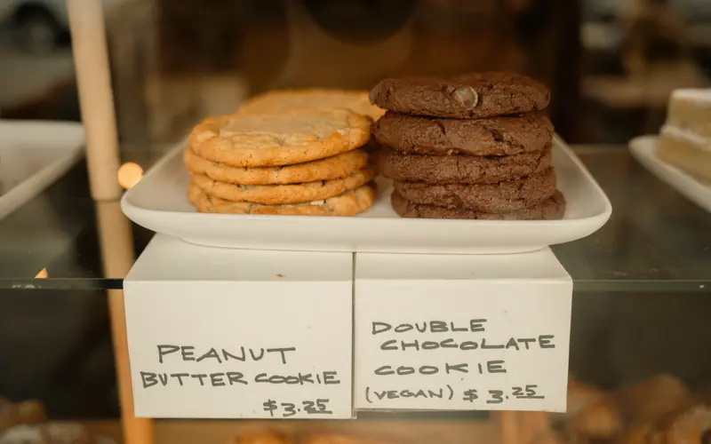 Stacks of peanut butter and chocolate cookies in a bakery case above handwritten price cards