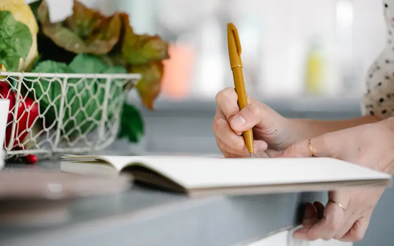 Hand writing notes in an open notebook on a kitchen counter