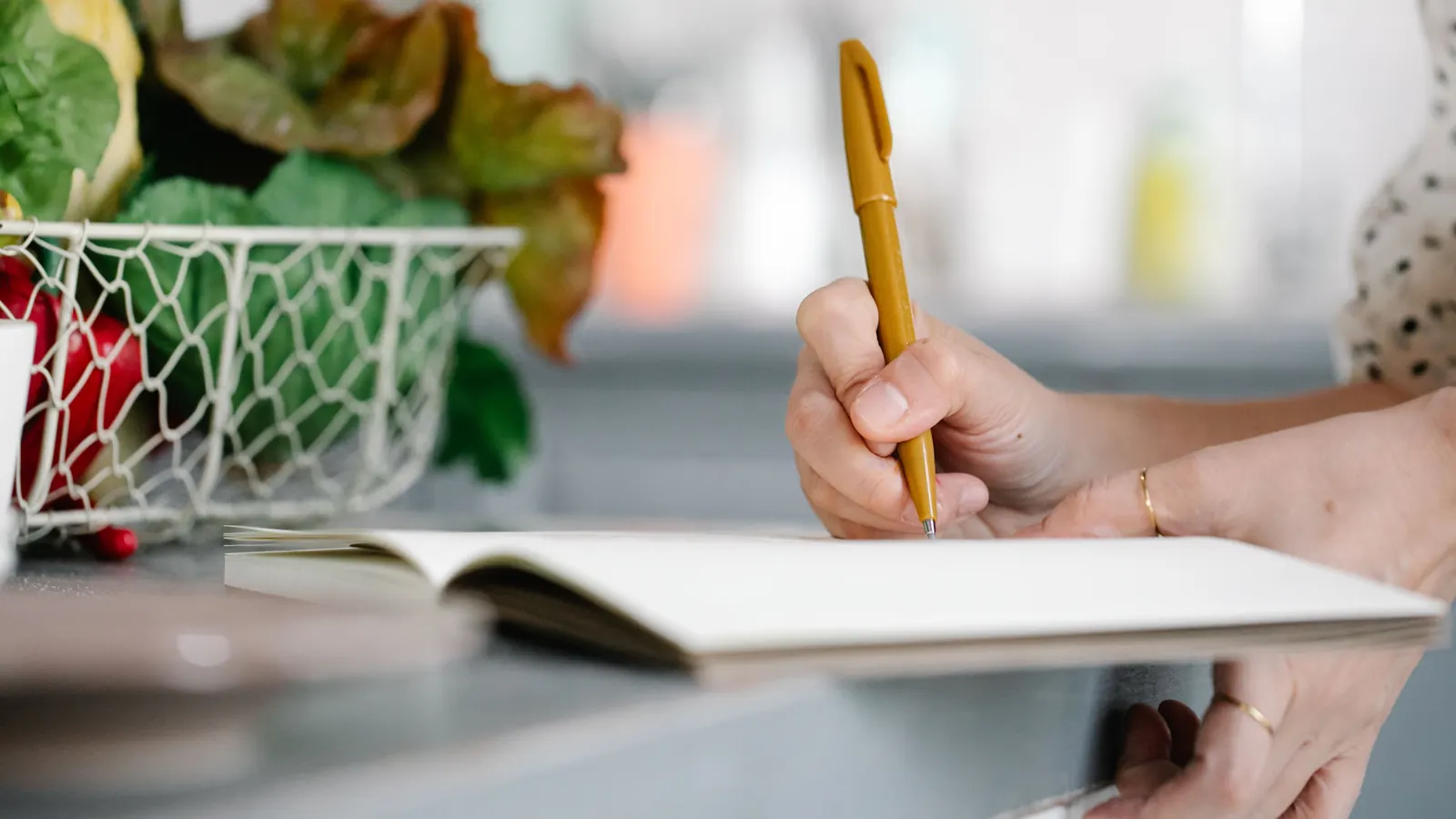 Hand writing notes in an open notebook on a kitchen counter