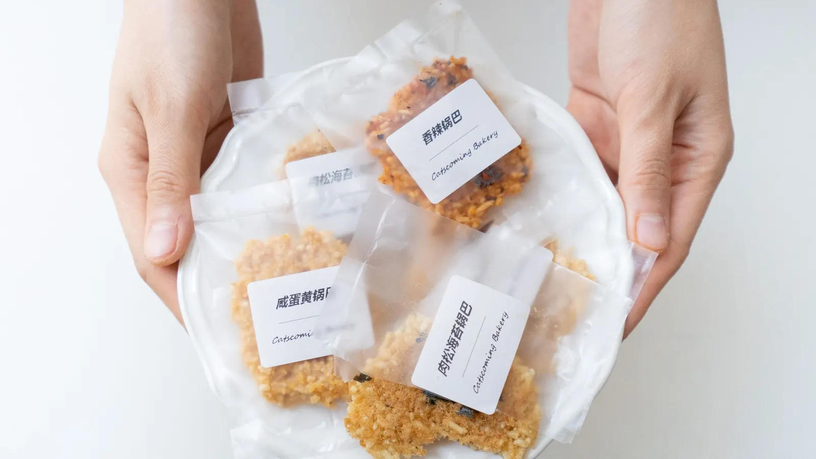 Hands holding a plate of individually bagged cookies, each bag with a printed white front label